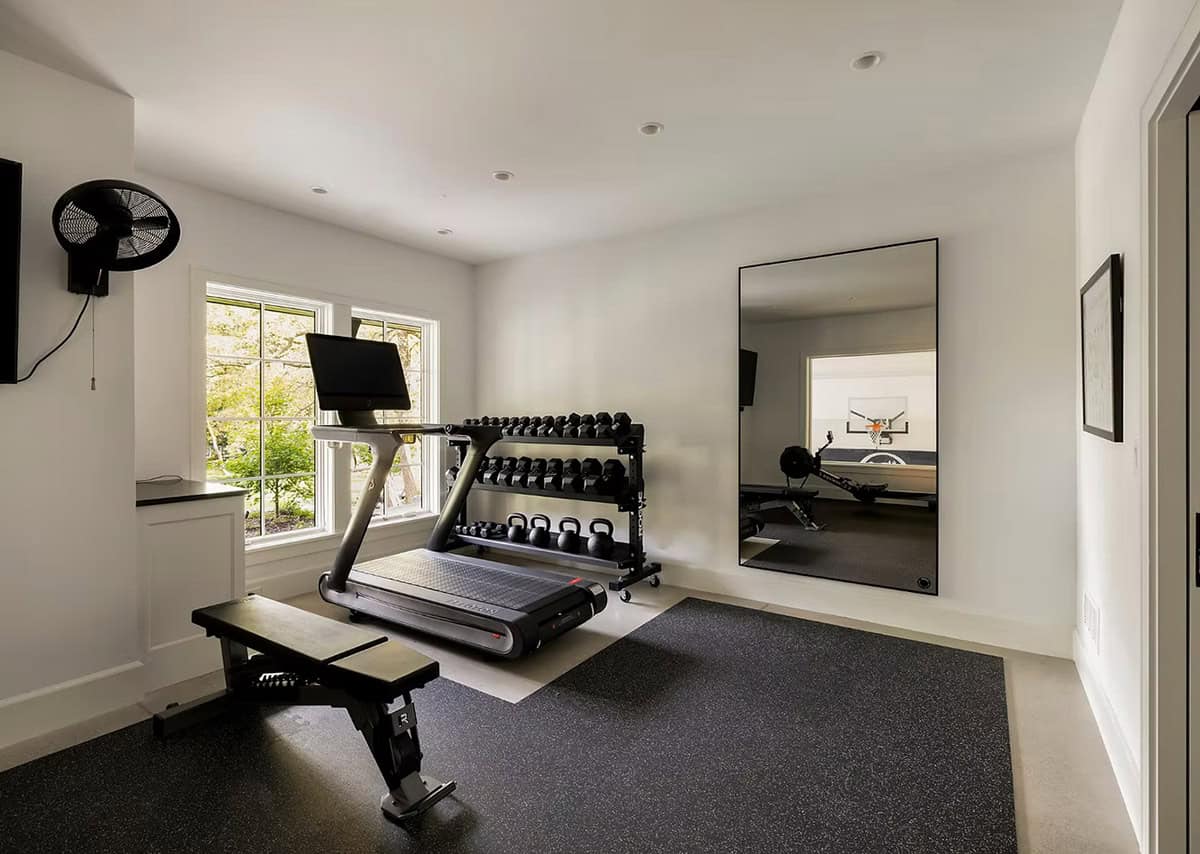 Home gym with a treadmill, dumbbell rack, weight bench and rubber flooring, with a mirror reflecting the sport court beyond