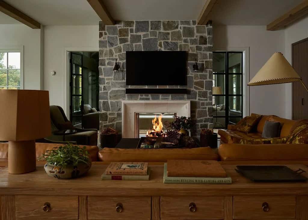Living room with a fire burning in the stone fireplace, a cognac leather sectional and an oak console table topped with vintage books