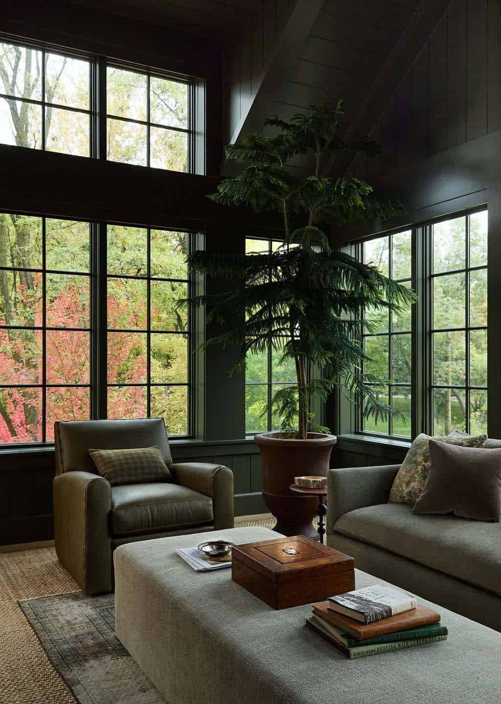 Green-paneled family room corner with a Norfolk pine in a terracotta urn, an olive leather armchair and a linen ottoman under tall windows