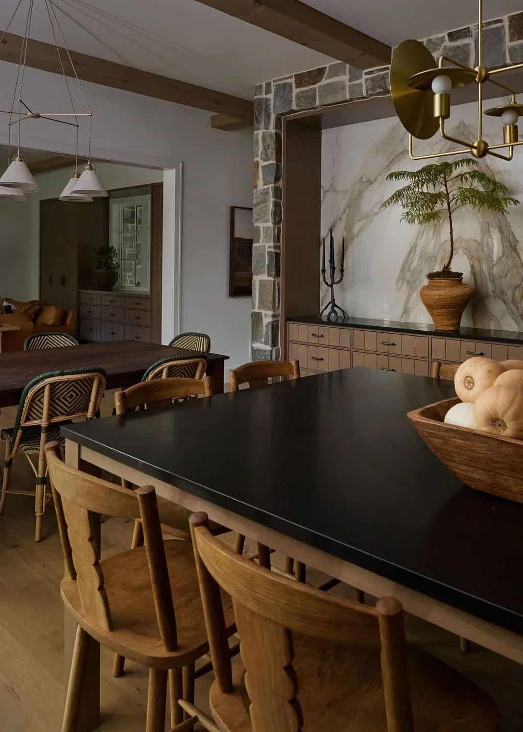 Black-topped kitchen island with wood counter stools looking toward the dining table and a stone-framed marble niche