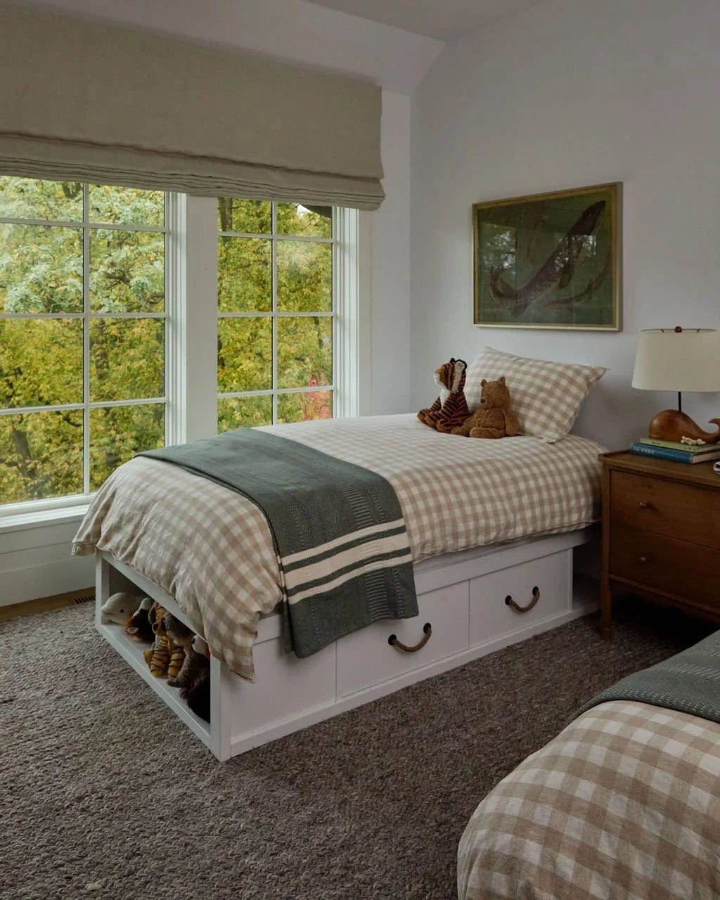 Boy's bedroom with twin beds in beige gingham, a storage bed with rope-pull drawers, a vintage fish print and windows to the trees