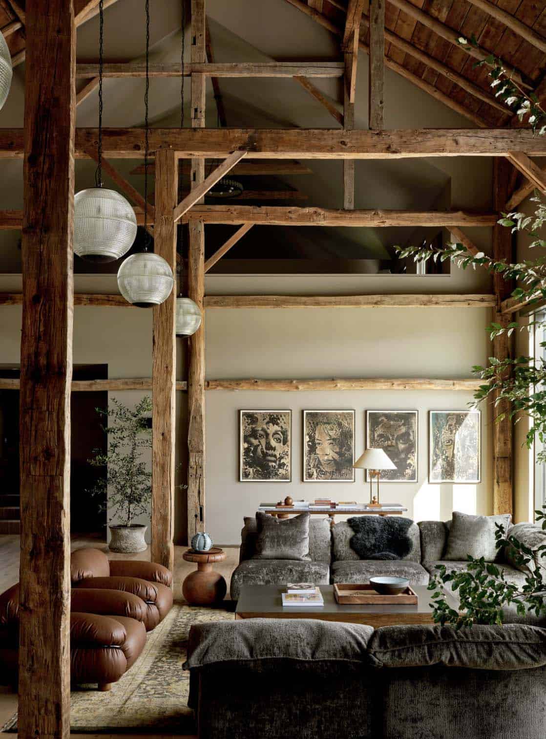 Barn great room with exposed timber frame, glass globe pendants, gray velvet sectional and brown leather lounge chairs