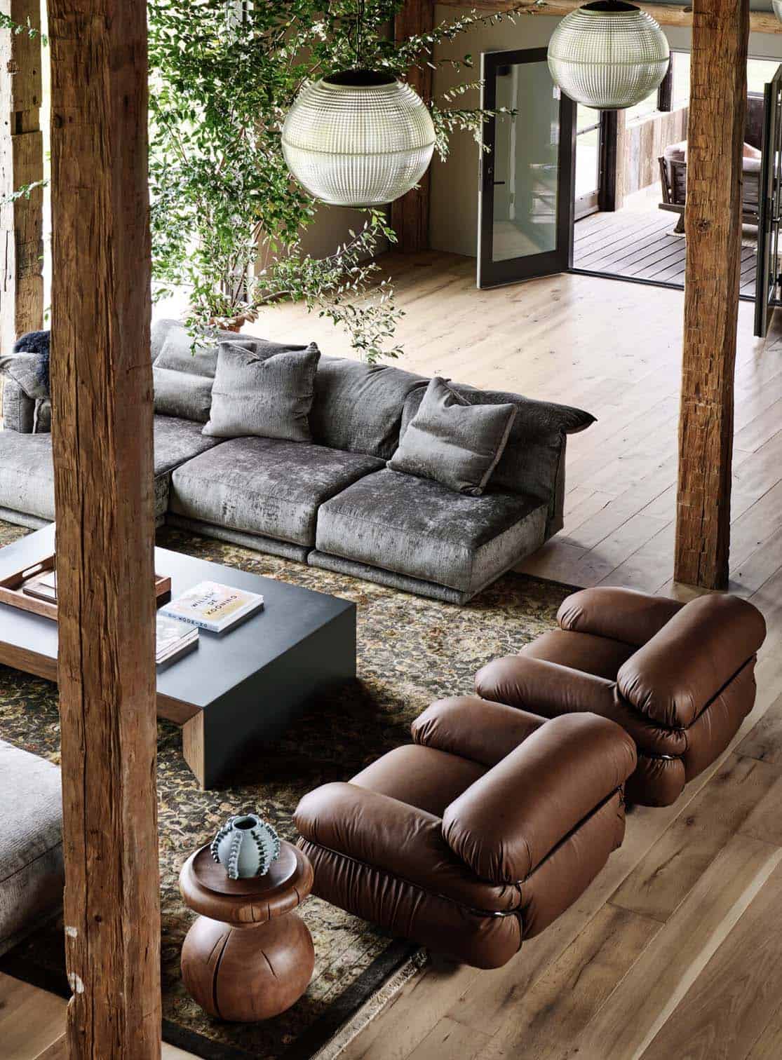Overhead view of brown leather lounge chairs and gray velvet sofa on a vintage rug between hand-hewn wood posts
