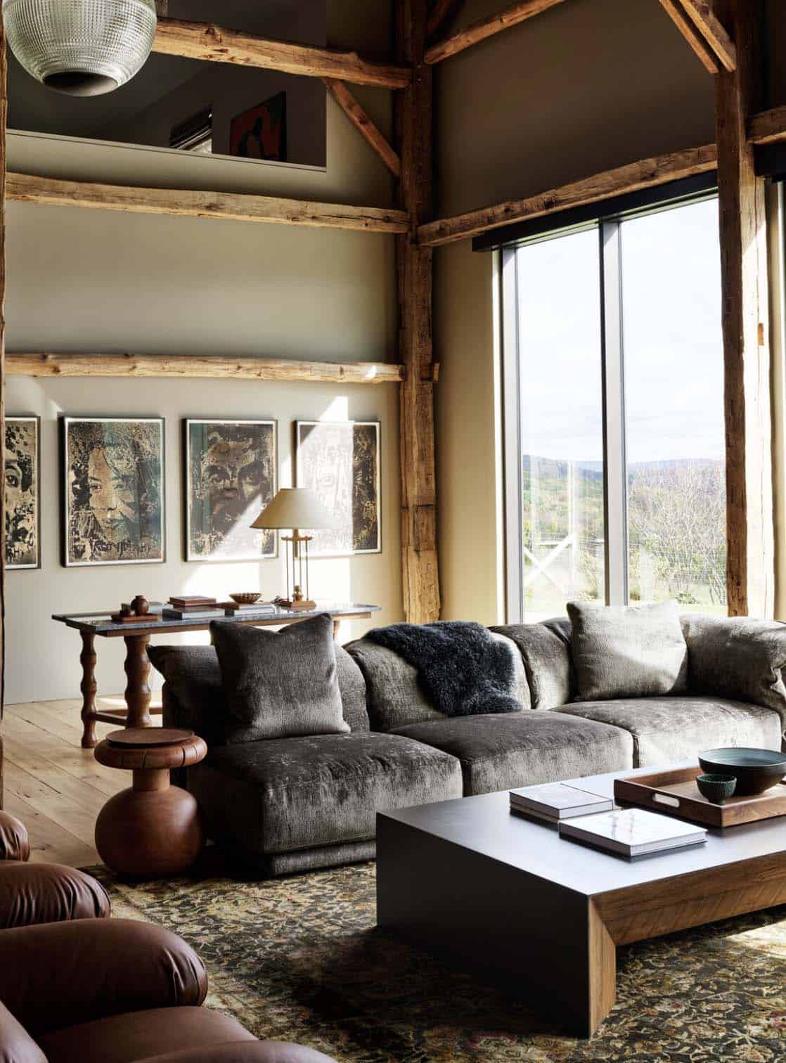 Living room with gray velvet sofa, four framed portrait prints and a tall window overlooking the hills