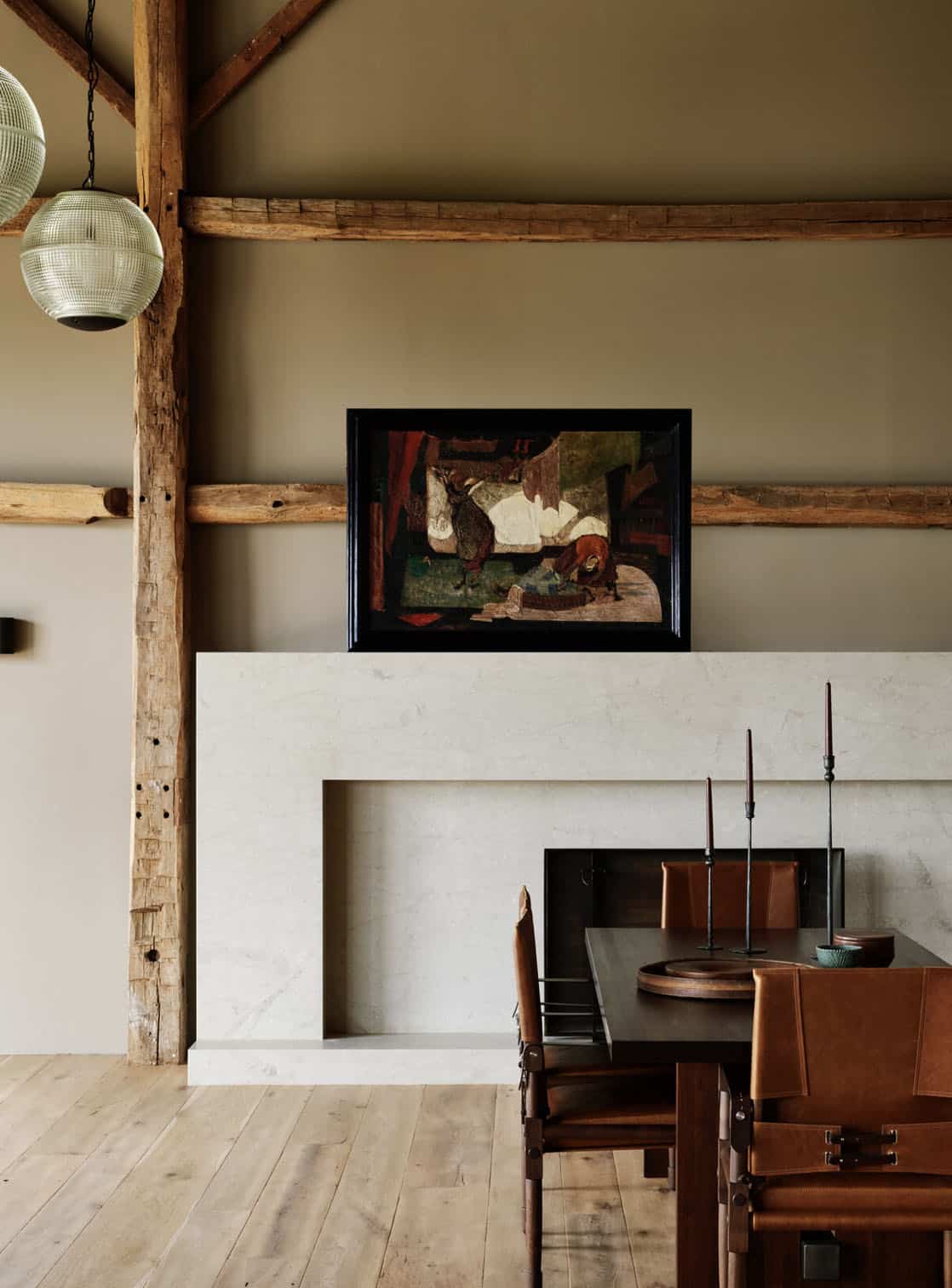 Pale stone fireplace with abstract painting on the mantel beside a dark wood dining table with leather chairs