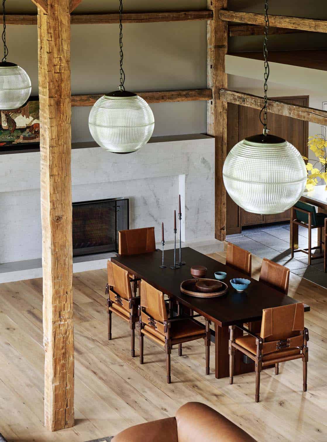 Dining area with leather safari chairs and dark wood table under glass globe pendants, stone fireplace behind