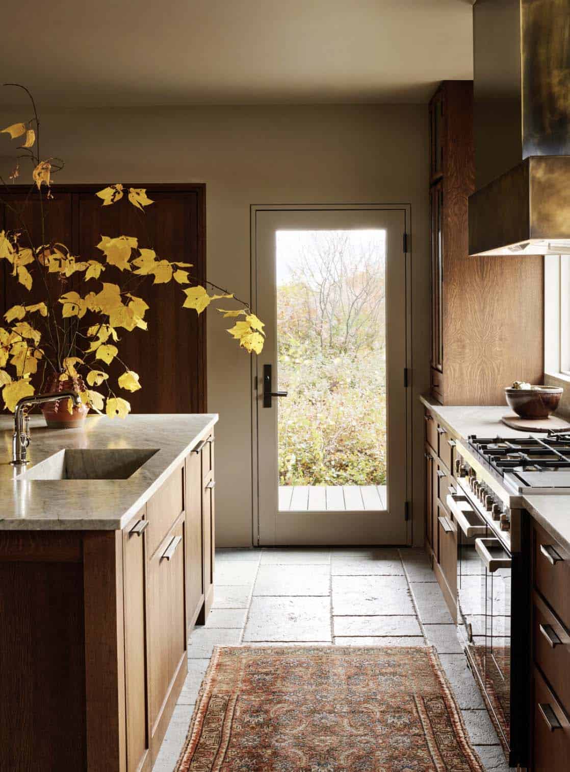 Kitchen with oak cabinetry, stone counters, tile floor, vintage runner and glass door to the garden