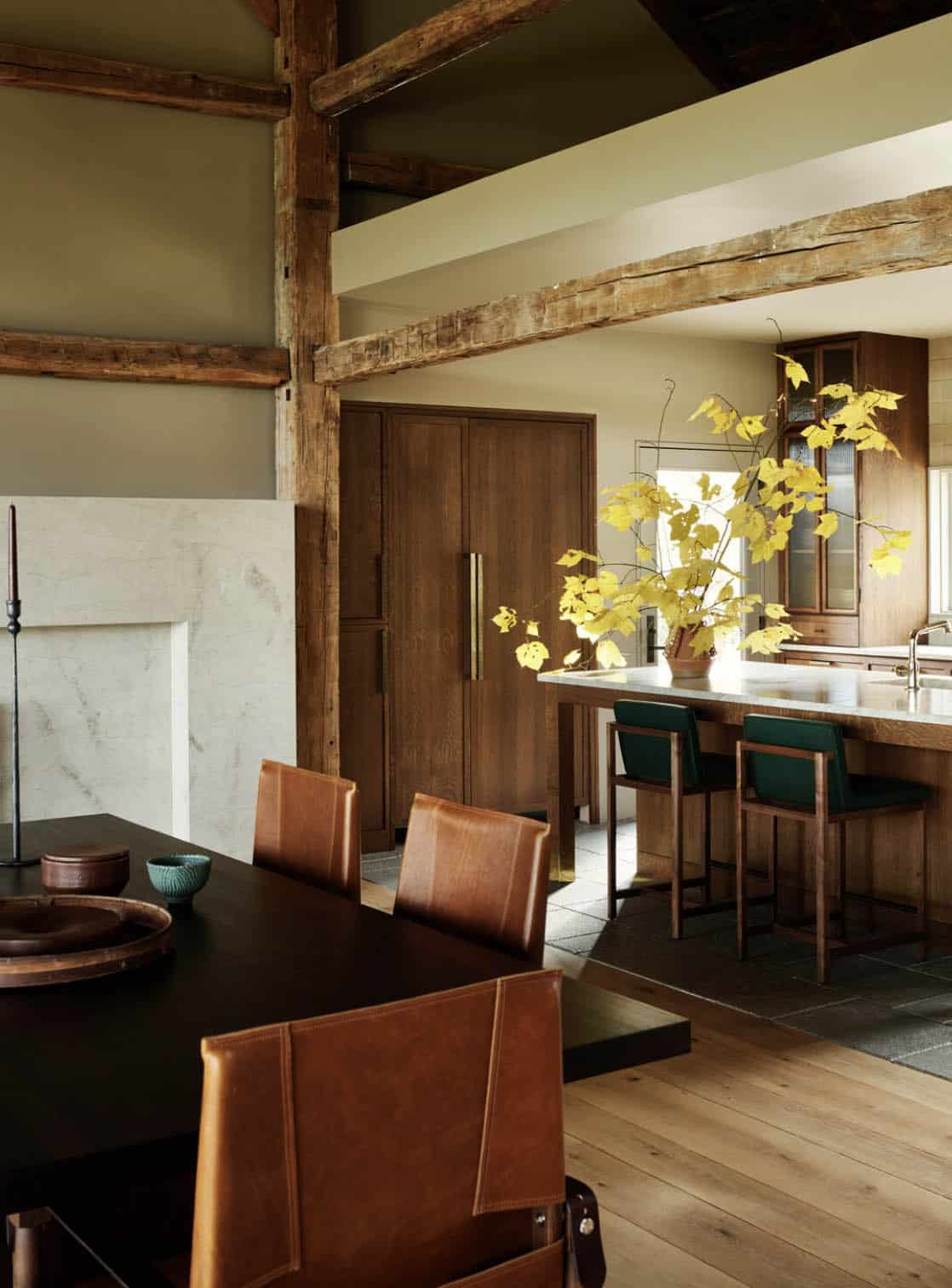 View from the dining table toward the kitchen island with green upholstered stools and yellow autumn branches