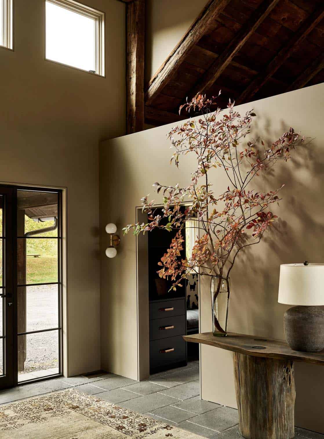 Entry with stone floor, double-height walls, live-edge console with lamp and a vase of autumn branches
