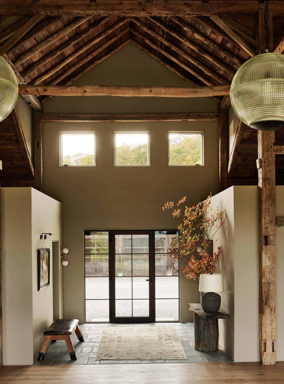 Entry hall under exposed roof timbers with clerestory windows, glass front door and a leather bench