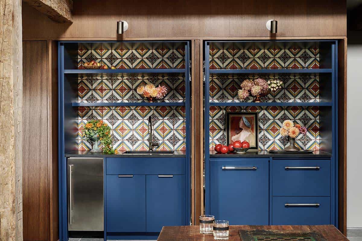 Hidden bar with blue cabinetry and colorful patterned tile, revealed behind open wood pocket doors
