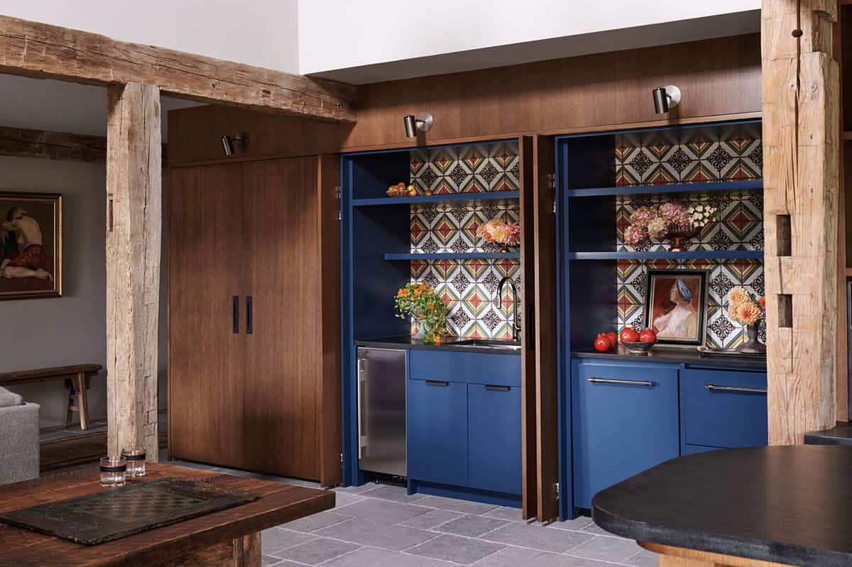 Wood-paneled wall with pocket doors open to a blue bar nook with patterned tile and a small sink