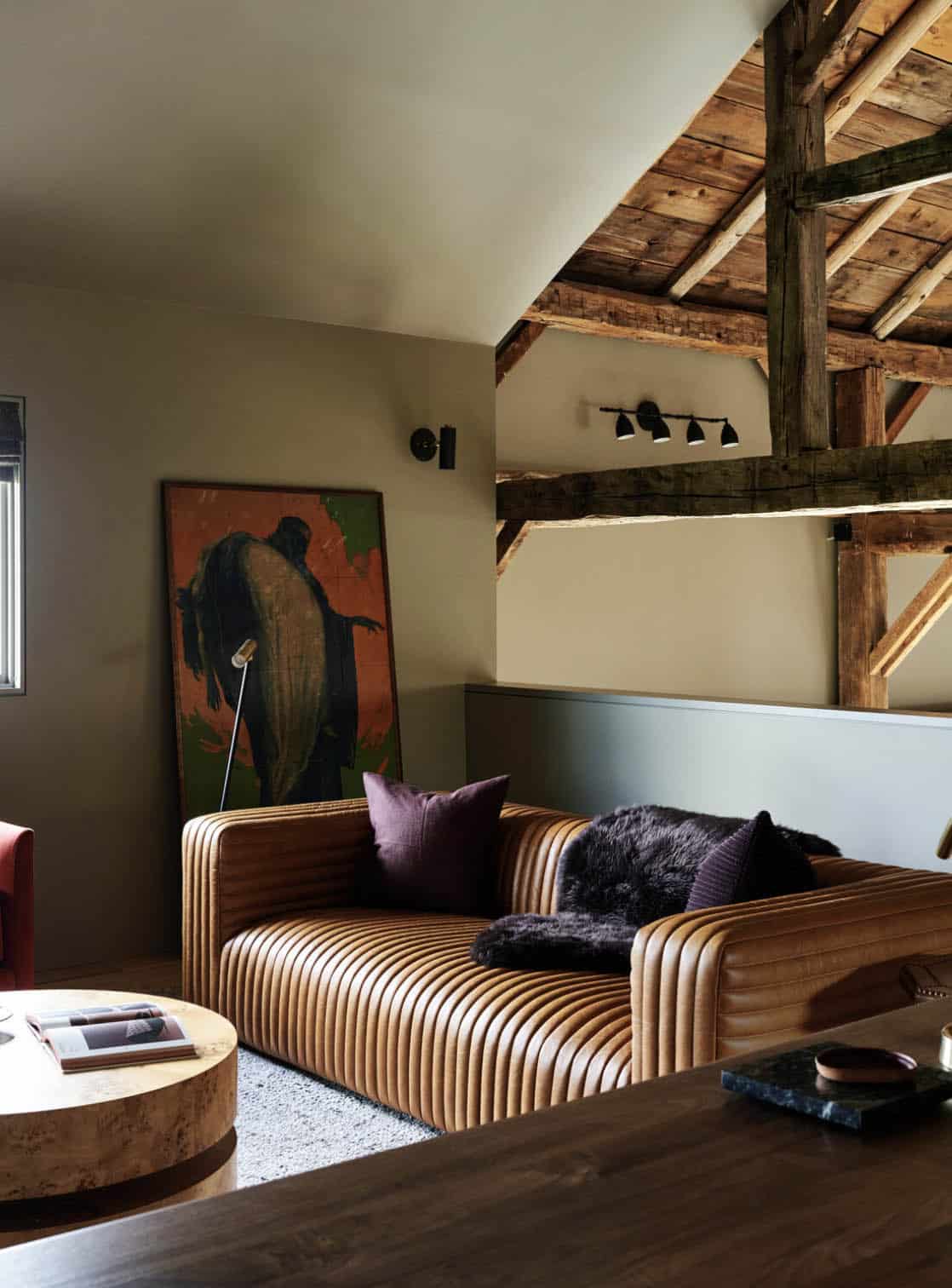 Loft lounge with channel-tufted cognac leather sofa, large leaning painting and exposed roof beams