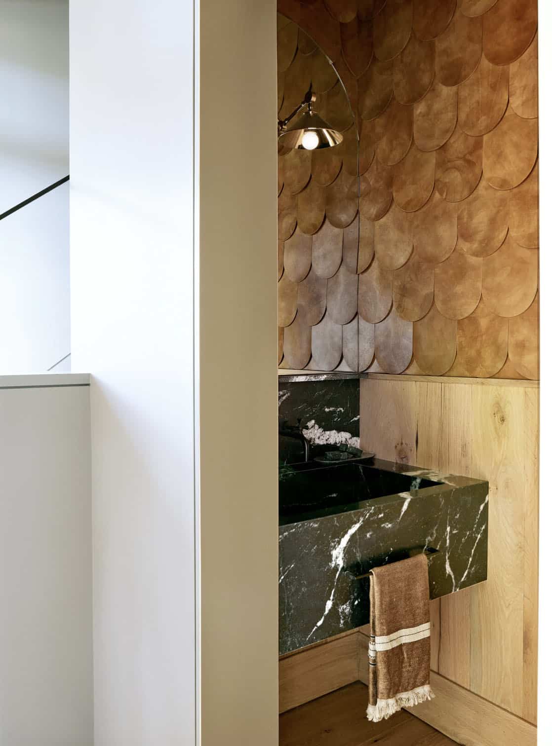 Powder room with black granite sink, oak paneling and scalloped leather wall tiles under a polished sconce
