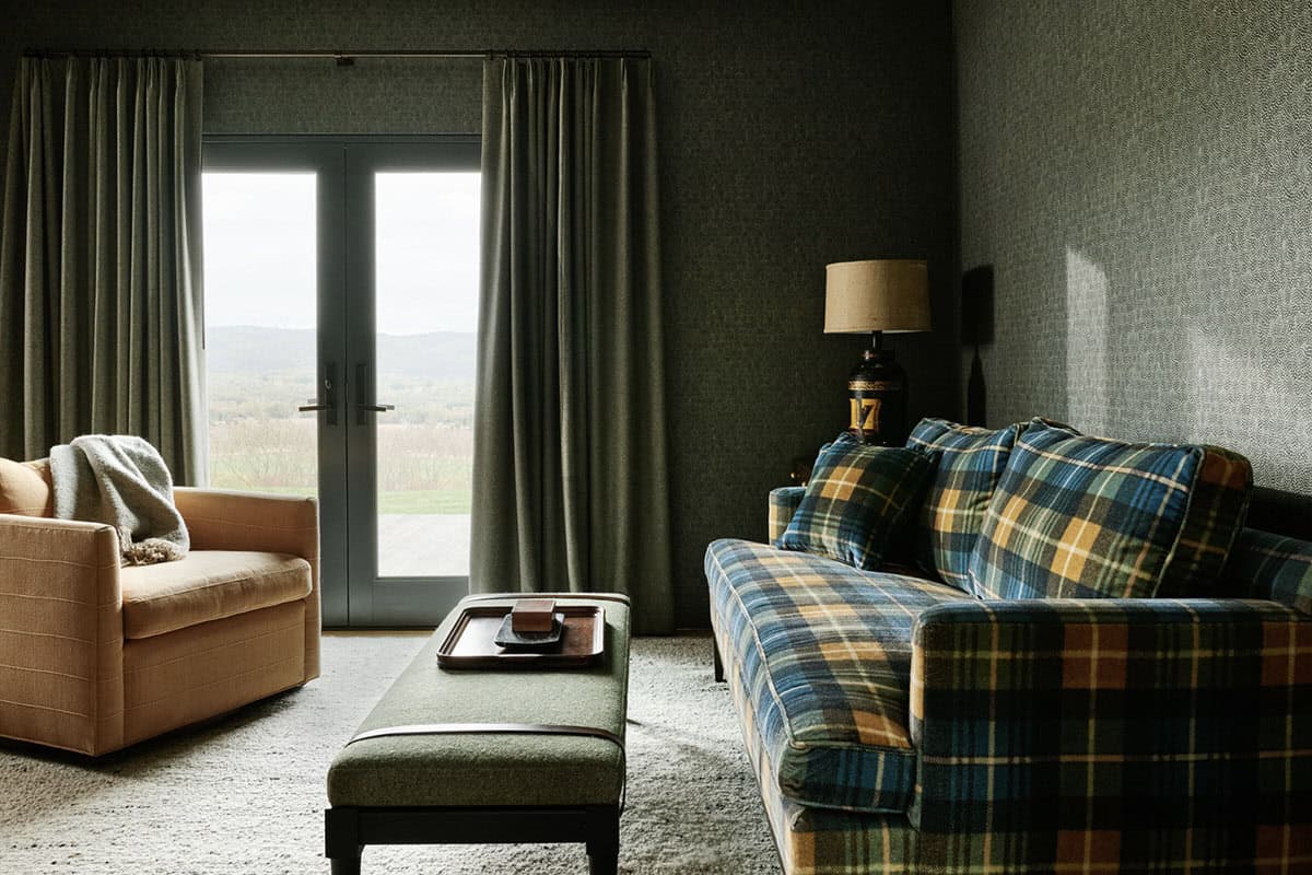 Den with plaid sofa, camel armchair, green ottoman and French doors opening to a valley view
