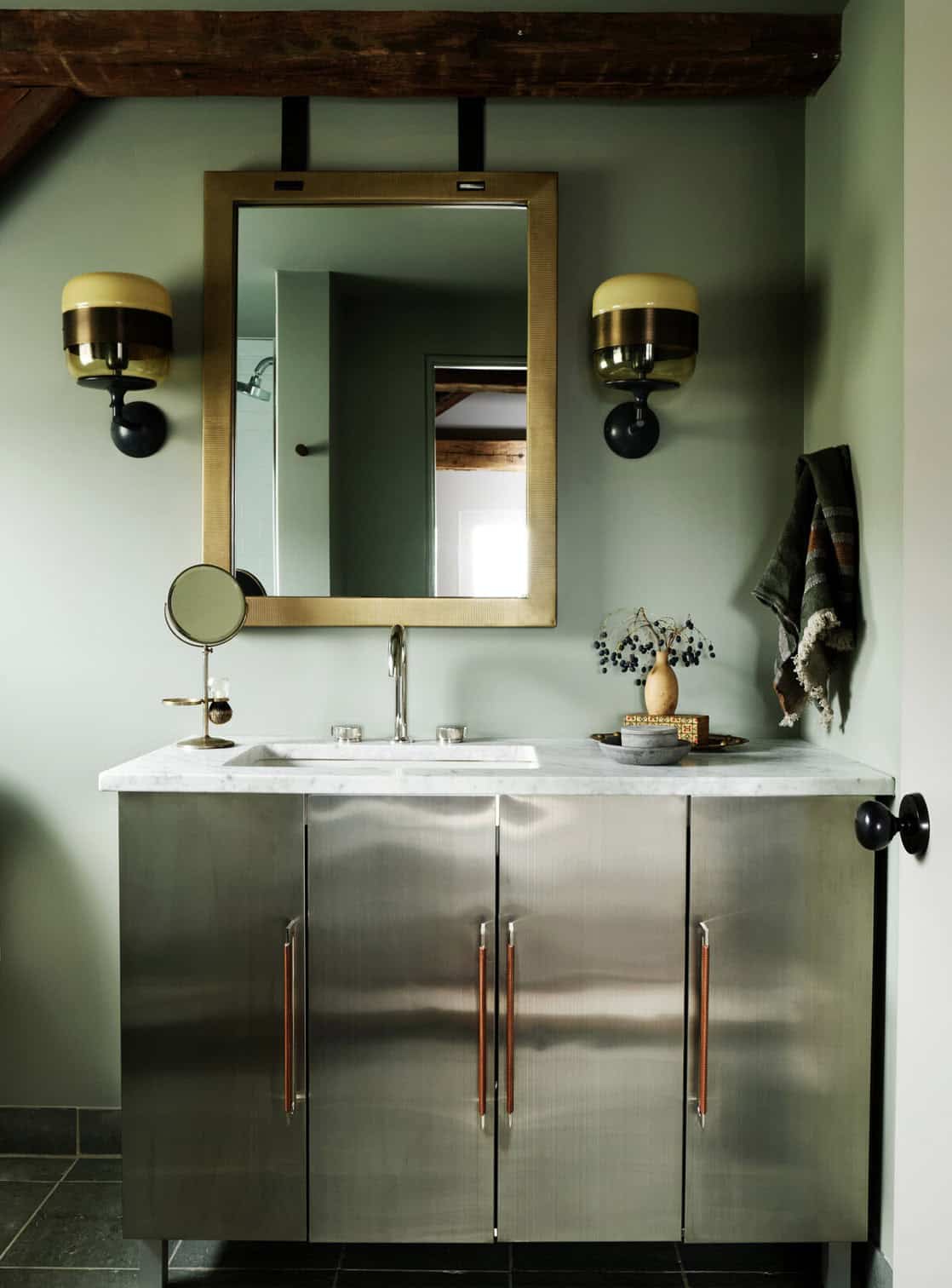 Sage green bathroom with stainless steel vanity, leather pulls, marble top, brass mirror and glass sconces