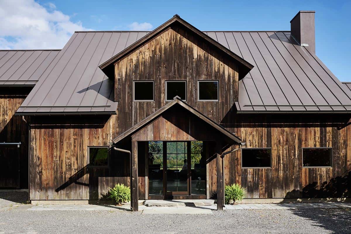 Barn exterior with weathered vertical wood siding, standing-seam metal roof and a gabled glass entry
