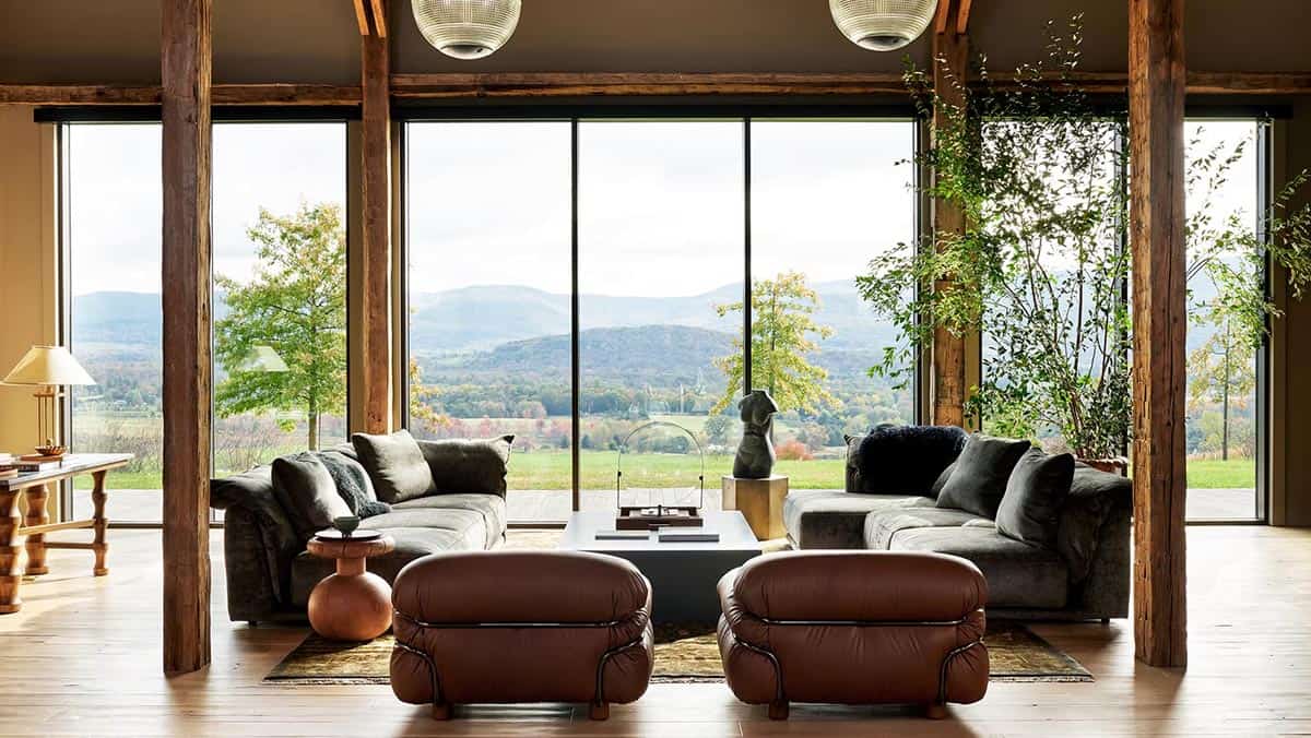 Great room with two gray velvet sofas and leather lounge chairs facing floor-to-ceiling windows and mountain views