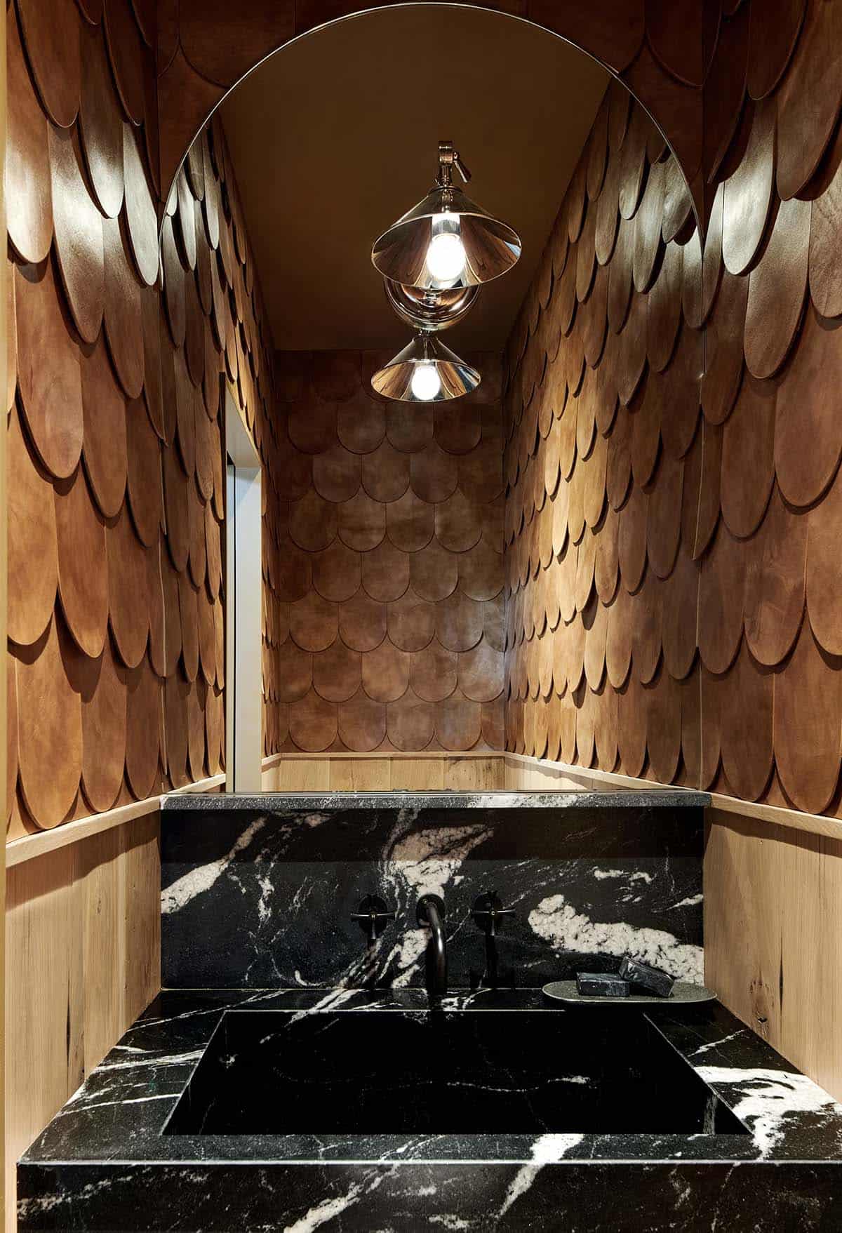 Powder room with black granite sink and arched mirror reflecting scalloped leather wall tiles and a cone sconce