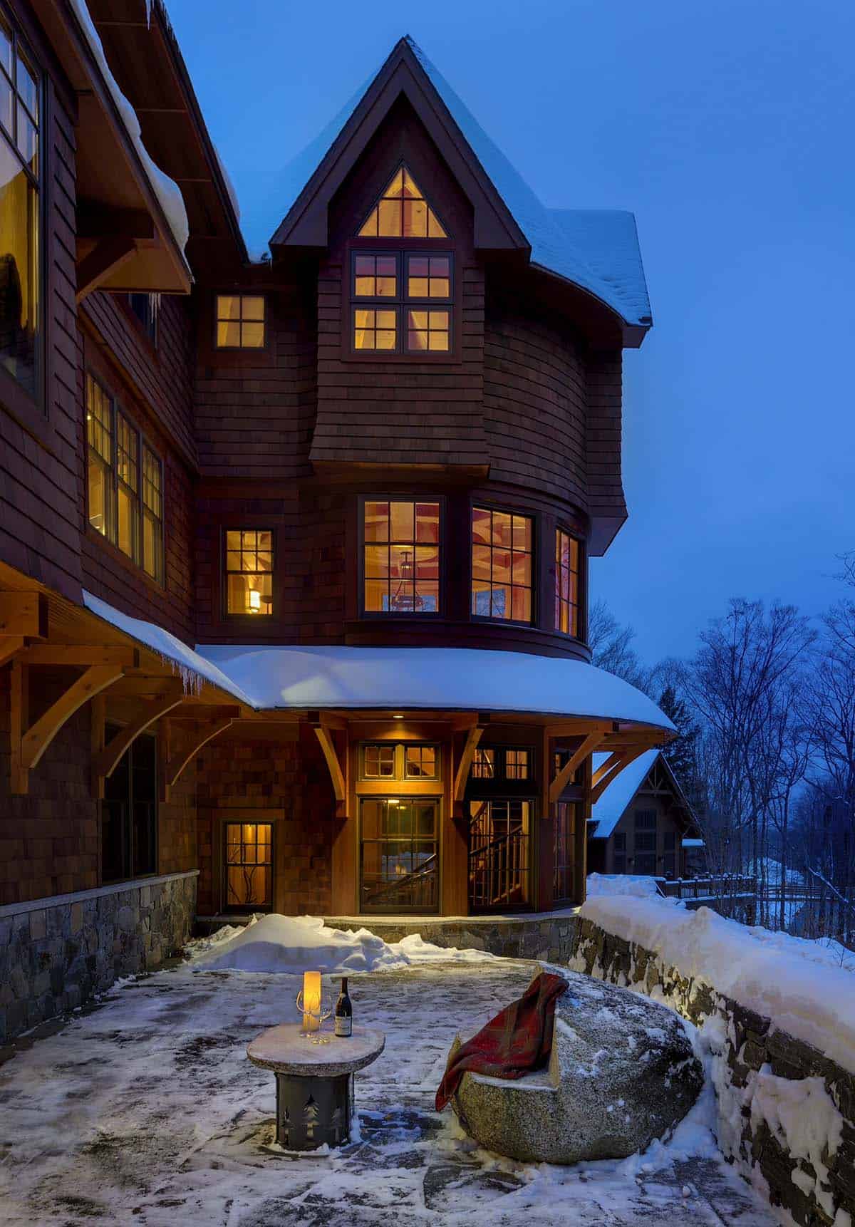 Cedar shingle turret with bay windows and a curved snow-covered roof on timber brackets above a stone terrace with a boulder seat