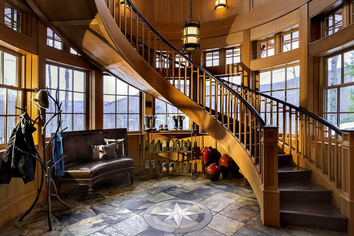 Round entry with a curving wood staircase, slate floor with an inlaid compass rose, leather bench and boot rack