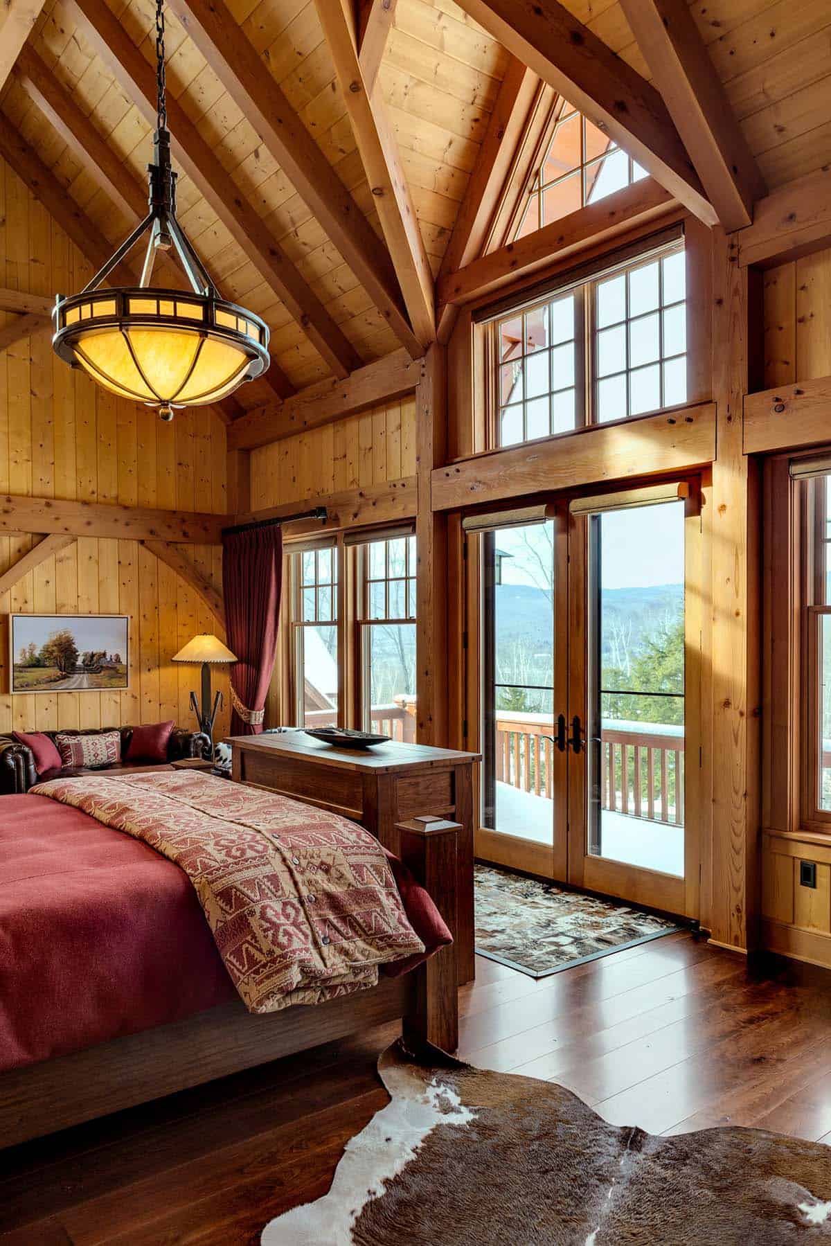 Bedroom with exposed timber trusses, a wrought-iron pendant and French doors opening to a snowy balcony with valley views