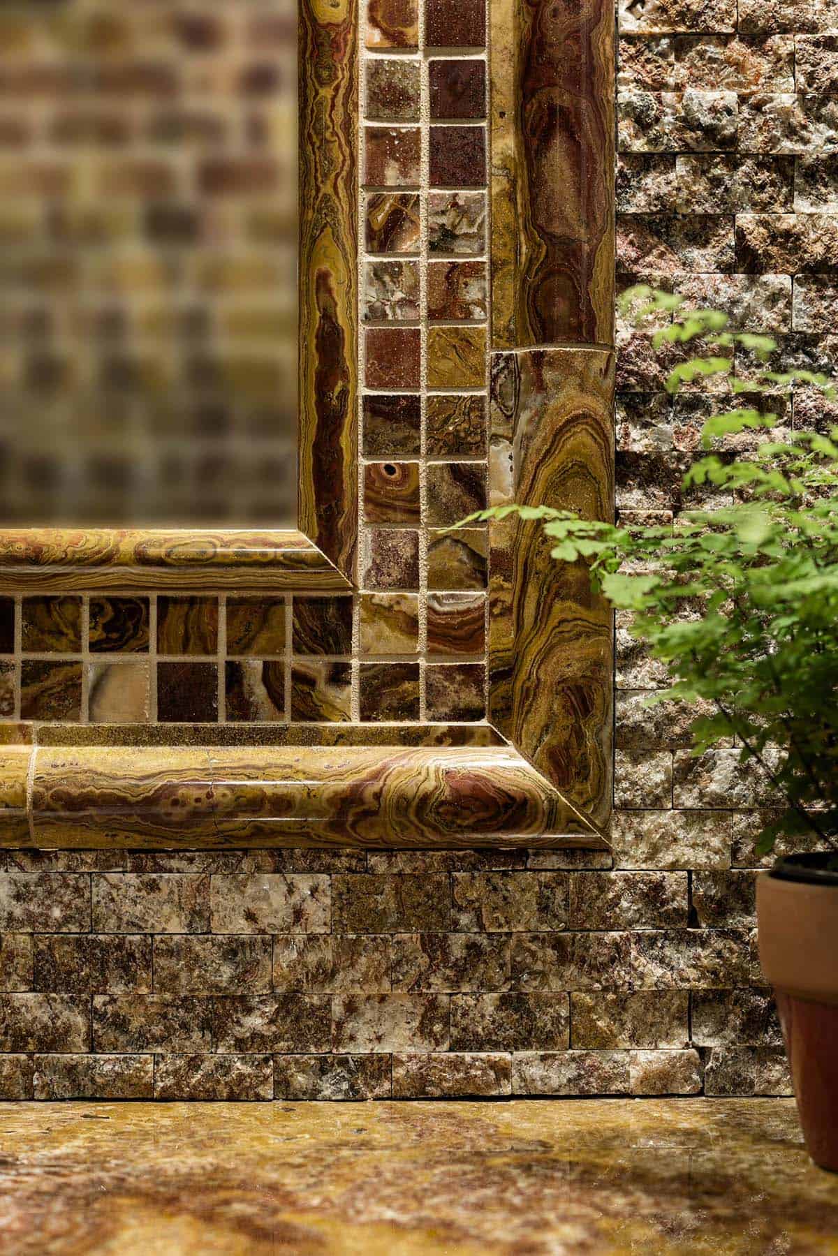 Close-up of a mirror framed in banded onyx and mosaic tile against a split-face stone wall
