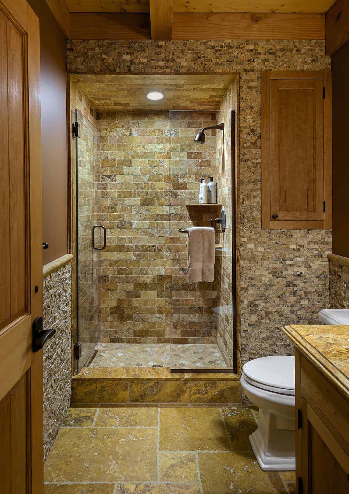 Bathroom with a travertine-tiled shower, split-face stone walls and a recessed wood cabinet