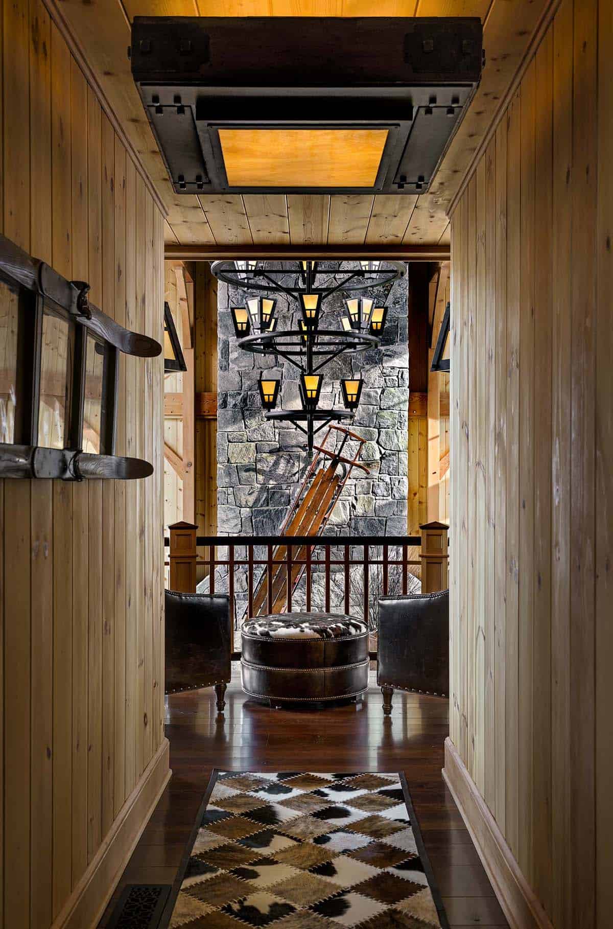 Hallway with a patchwork cowhide runner leading to leather chairs and a sled leaning against a stone chimney