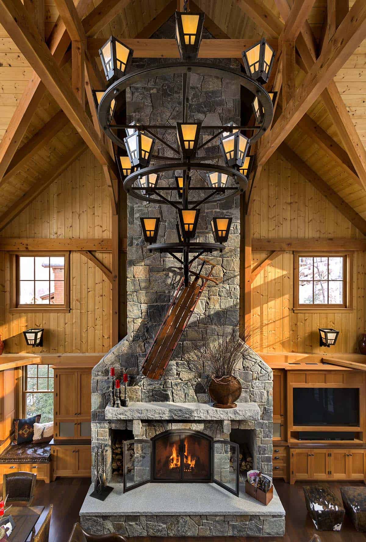 Stone fireplace rising to a timber-framed ceiling, with a tiered wrought-iron chandelier and an antique sled
