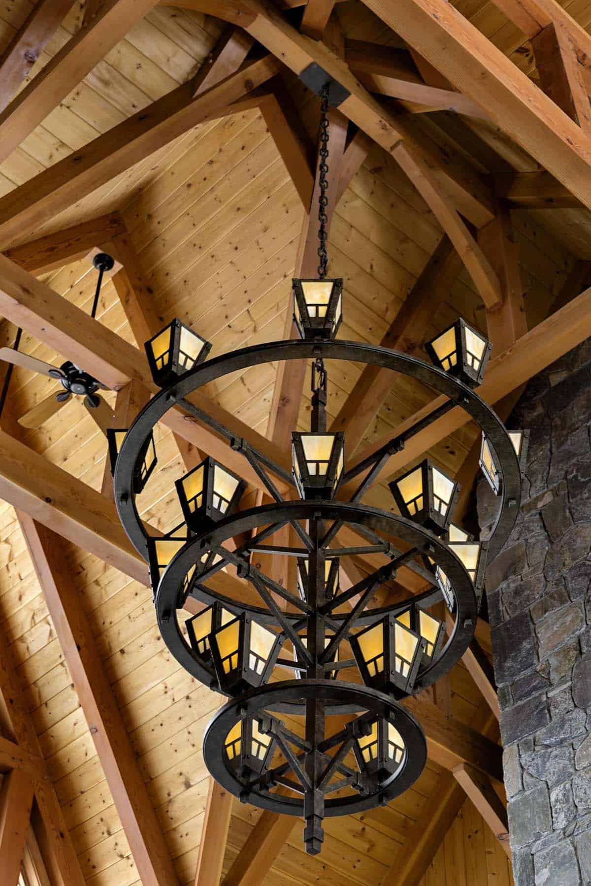 Three-tier wrought-iron chandelier with lantern-style lights beneath exposed timber trusses