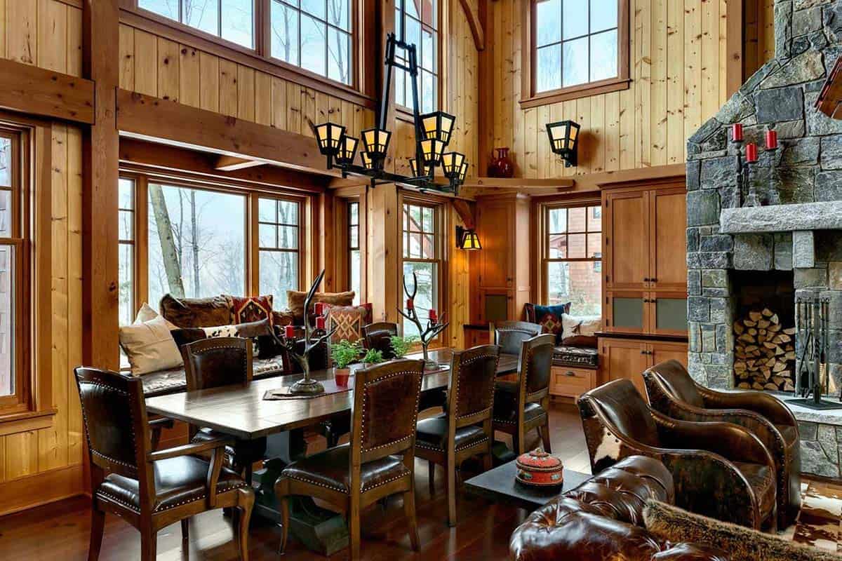 Dining area with a plank table, leather chairs, a linear lantern chandelier and a window seat with pillows