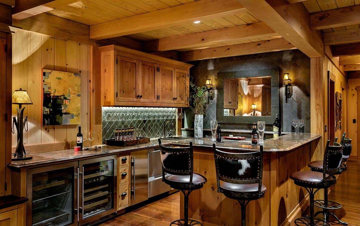 Lower-level bar with knotty wood cabinets, diagonal slate backsplash, hanging glassware and beverage refrigerators