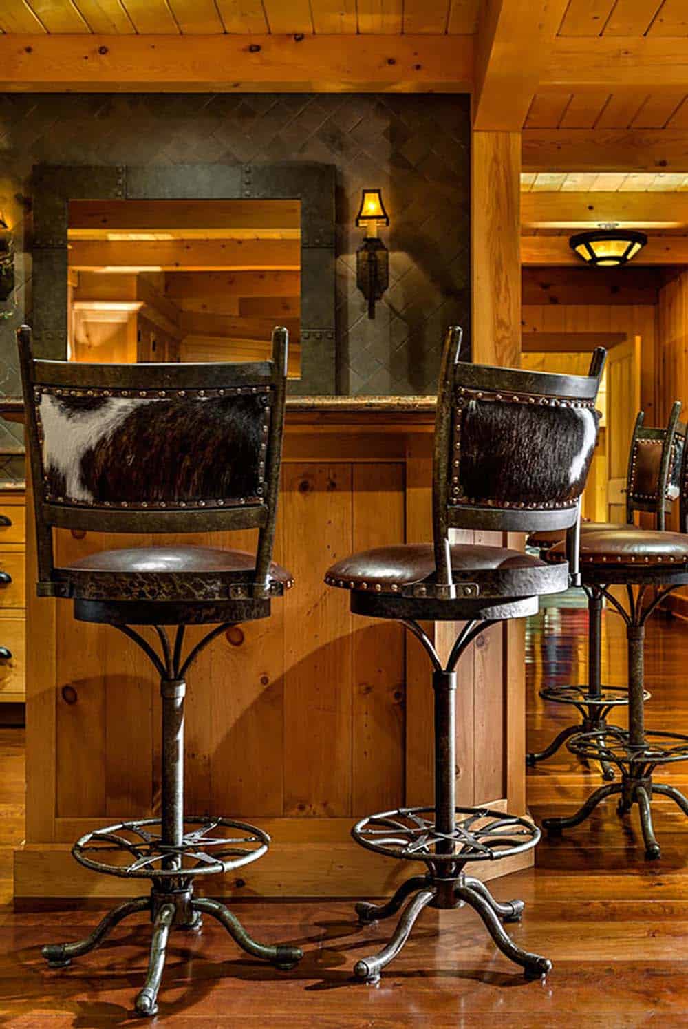 Cowhide and leather swivel bar stools on iron bases in front of a riveted metal mirror