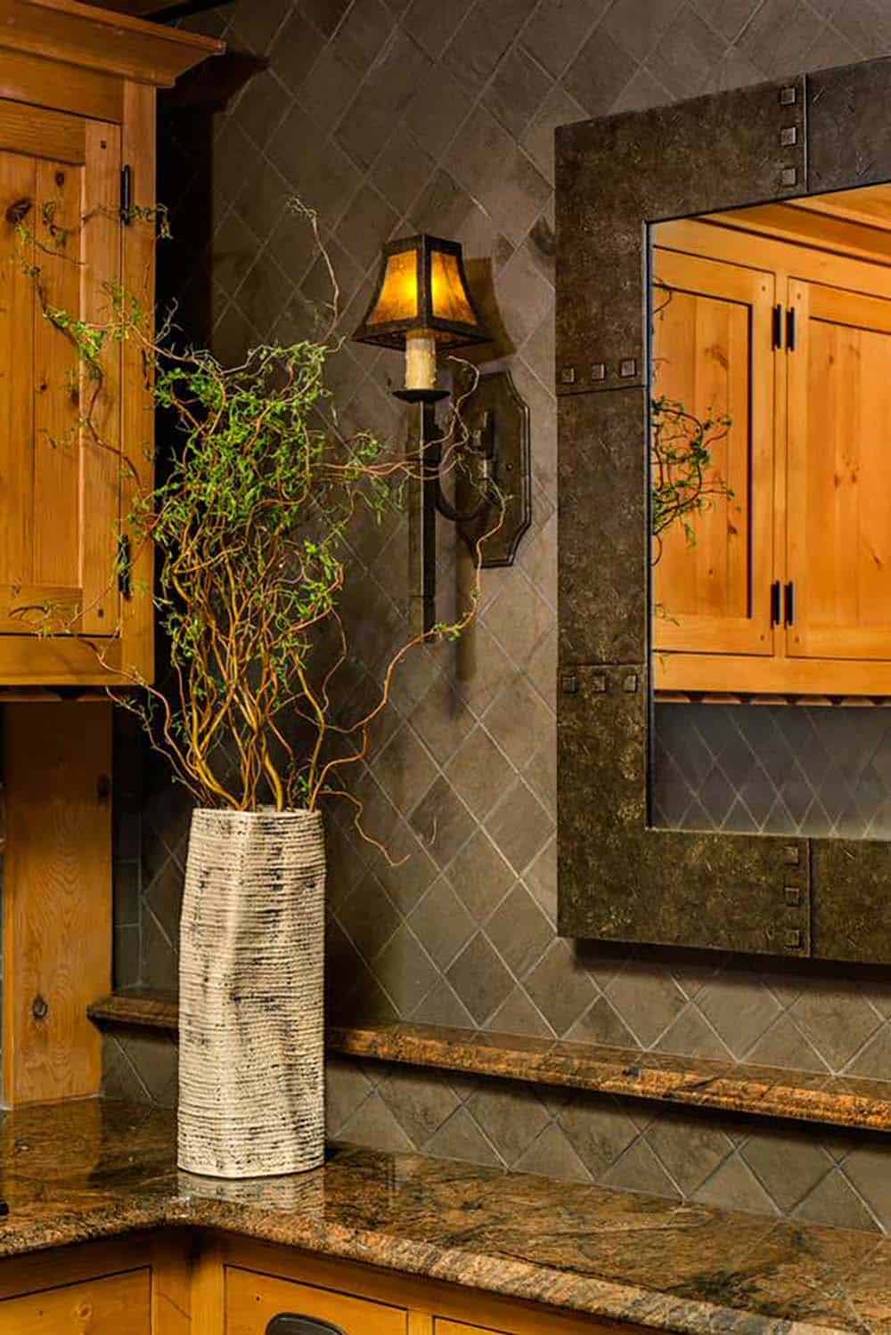 Mica-shaded sconce, riveted metal mirror and diagonal slate backsplash beside a vase of curly willow