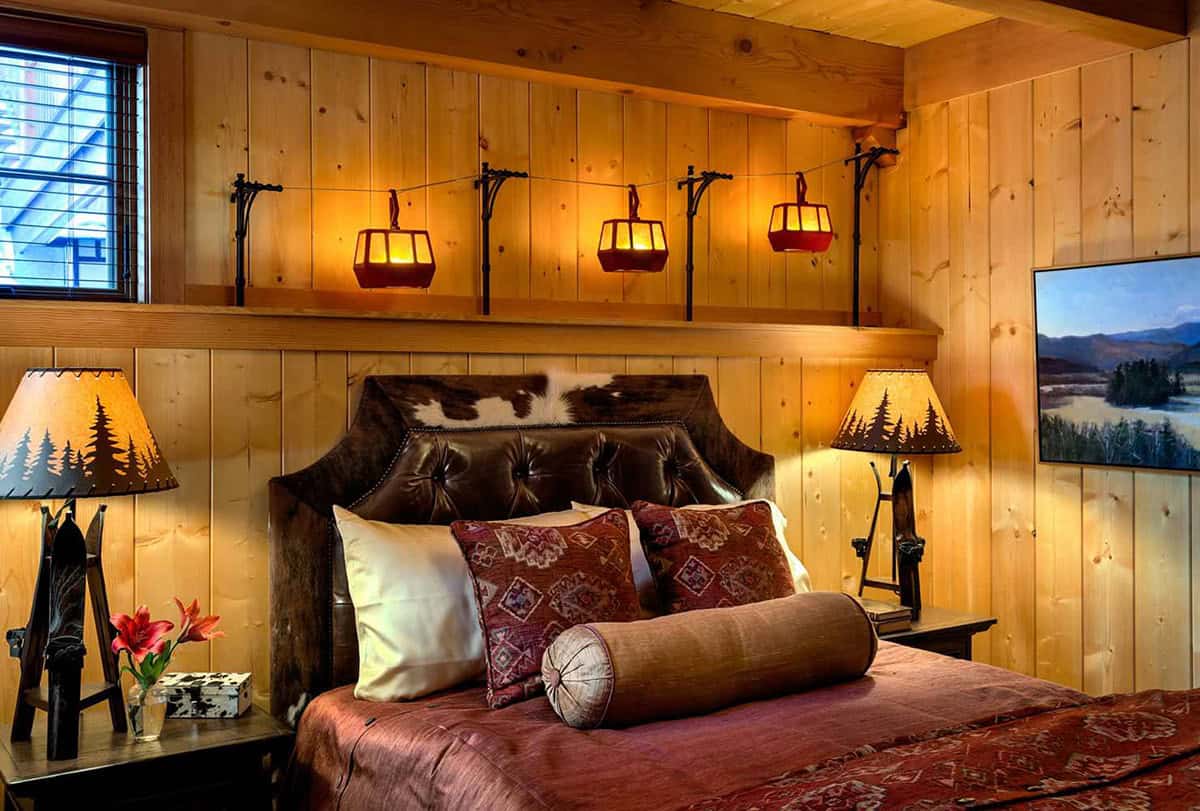 Guest bedroom with miniature gondola lights above a cowhide headboard and pine-tree lamps on ski-leg bases