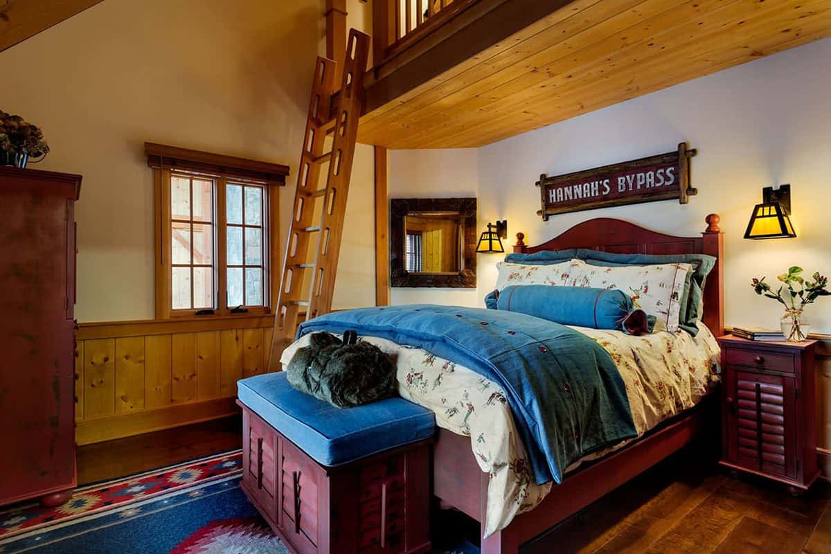 Child's bedroom with a red-painted bed, wooden ladder to a loft, Hannah's Bypass ski trail sign and blue bedding