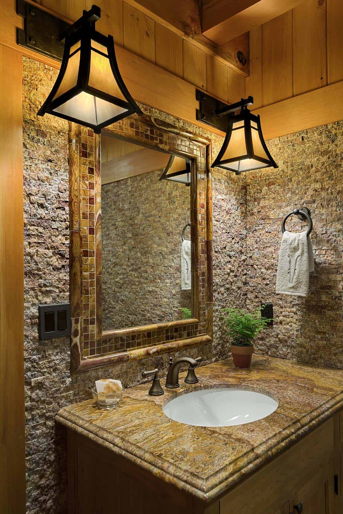Powder room vanity with onyx and mosaic-framed mirror, split-face stone walls, swirled stone countertop and mica pendant lights
