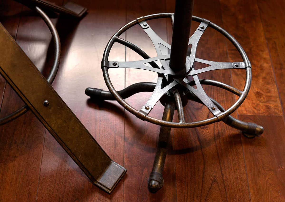 Close-up of an iron bar stool footrest with star-shaped spokes on a cherry wood floor