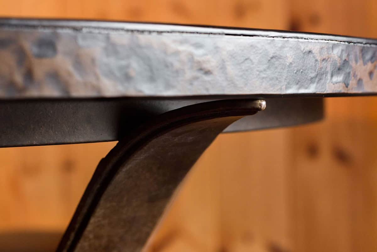 Close-up of a hand-hammered metal tabletop edge resting on a curved iron base
