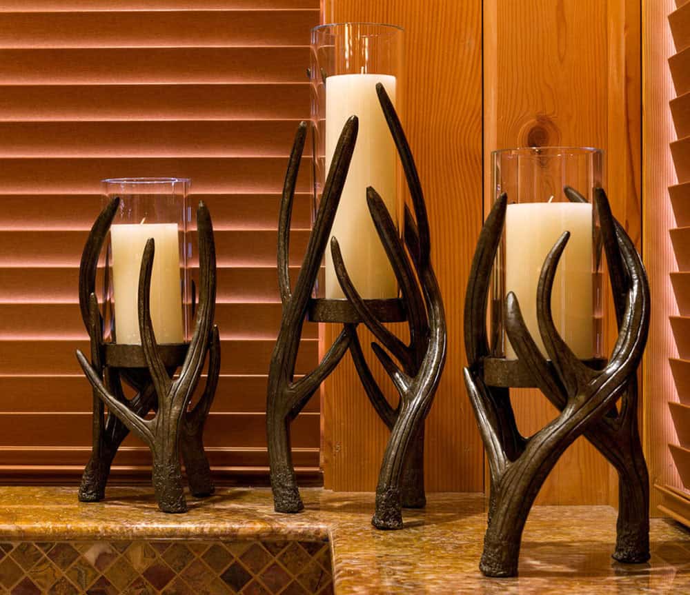 Three antler-style candle holders with glass hurricanes and white pillar candles on a stone ledge