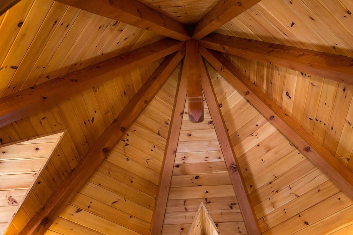 Looking up at a knotty pine ceiling with timber beams radiating from a central king post