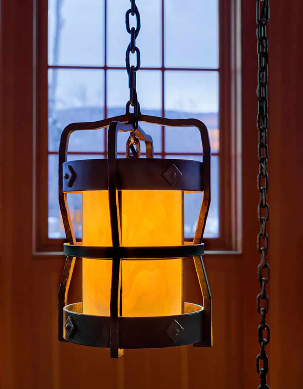 Iron cage lantern pendant with amber glass hanging from a chain in front of a window