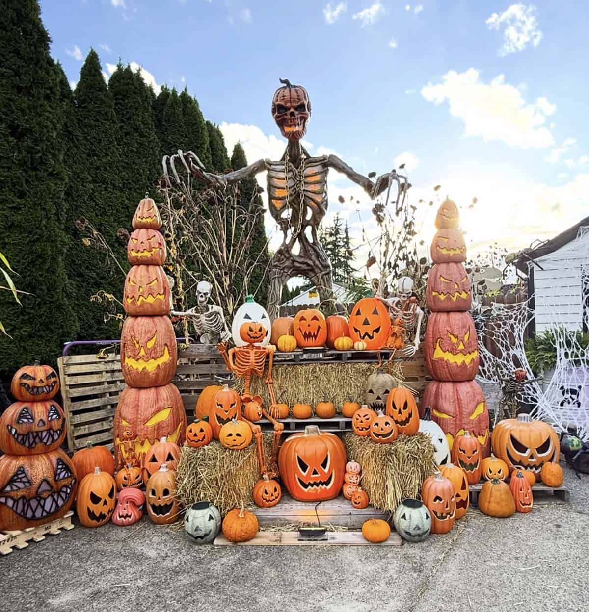 Tiered pallet and hay bale display with stacked jack-o'-lantern towers, a giant pumpkin-headed skeleton, and small skeletons