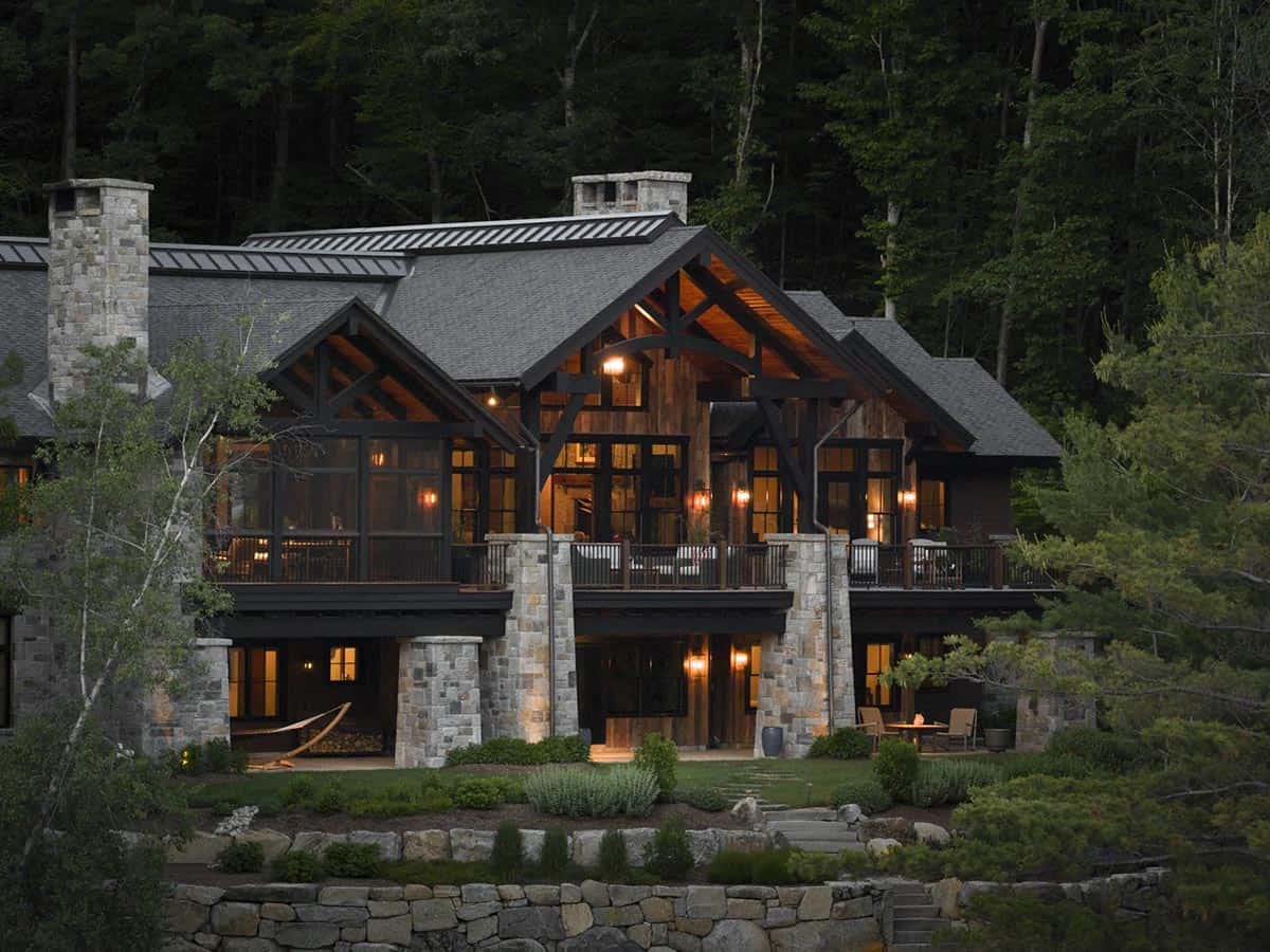 Lake-facing side of the house lit at dusk, with stone piers, a long upper deck, a screened porch and stone retaining walls below