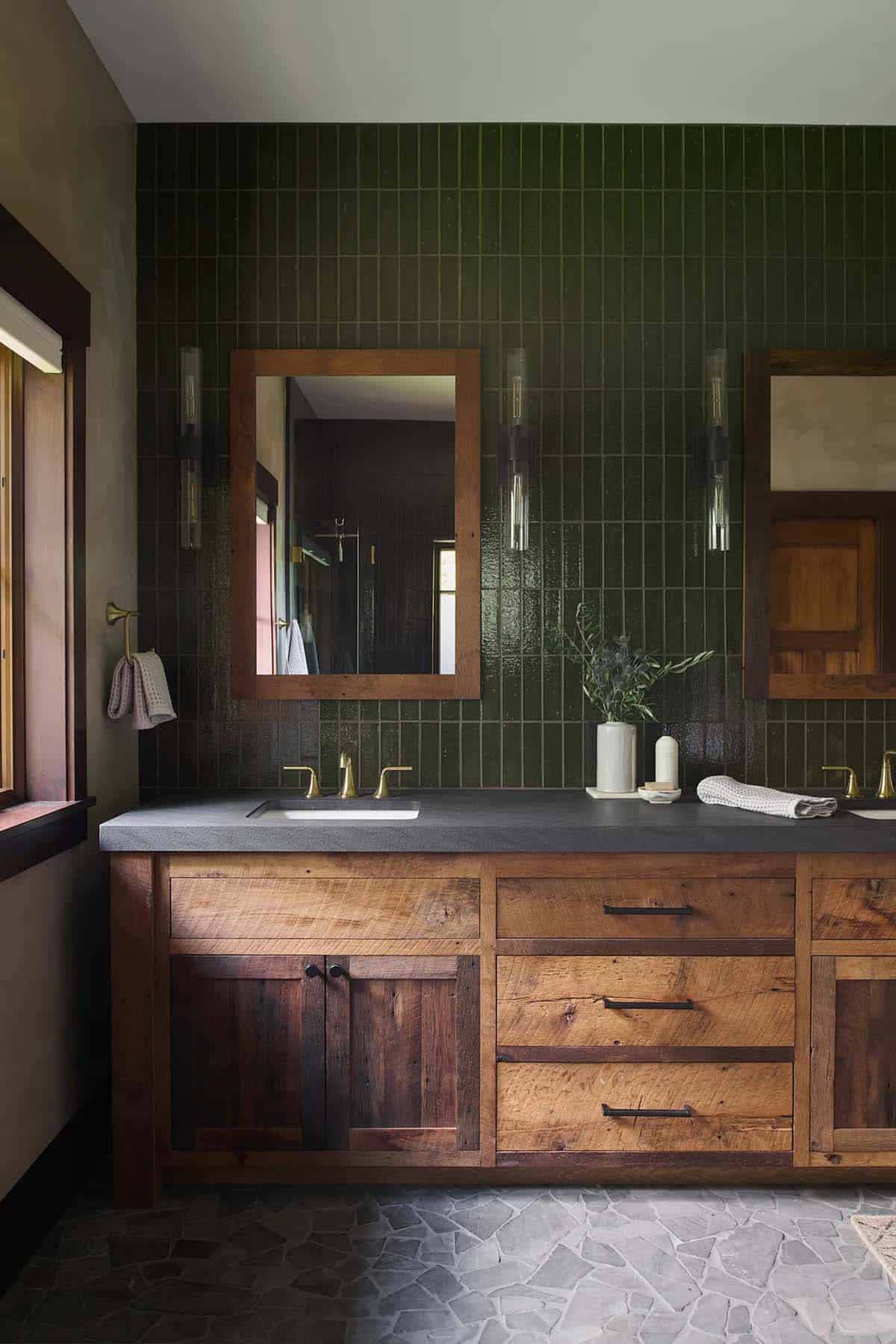 Bathroom vanity in reclaimed wood with a dark stone top, brass faucets, glass sconces, wood-framed mirrors and green vertical tile