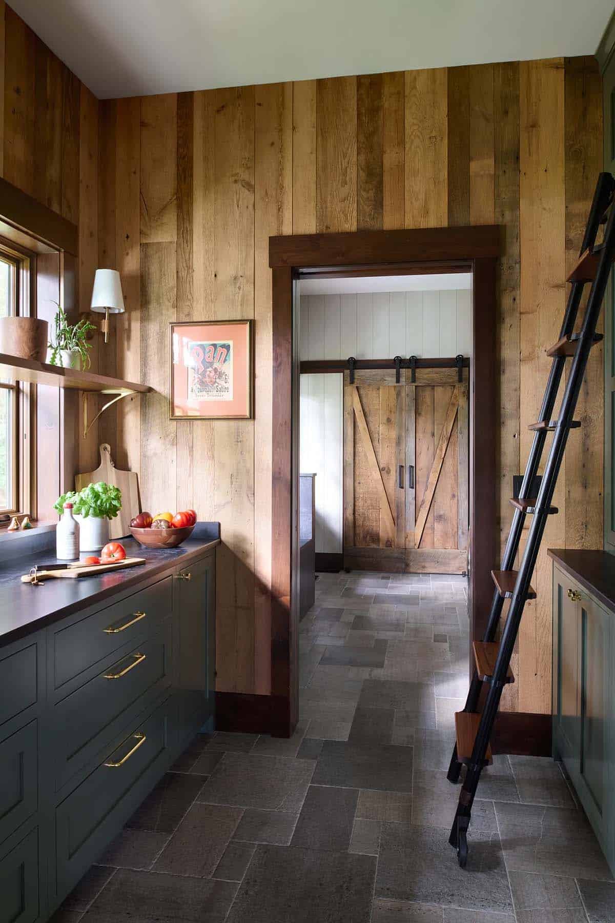 Pantry with reclaimed wood walls, dark green cabinets with brass pulls, a rolling library ladder and a doorway to a room with barn doors
