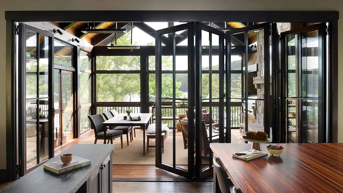 Folding glass doors partly closed between the kitchen and the screened porch overlooking trees and the lake