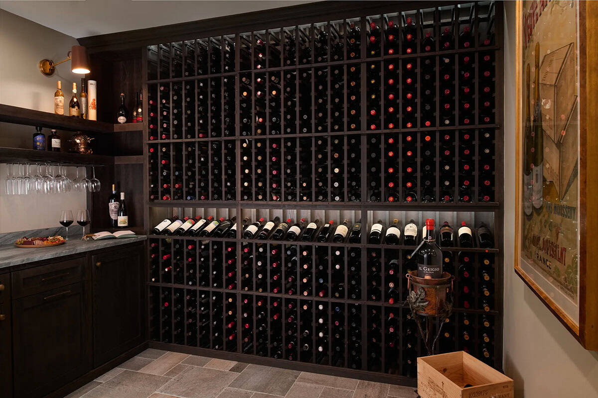 Wine room with floor-to-ceiling dark wood wine racks, a stone-topped counter with stemware, and a framed vintage poster