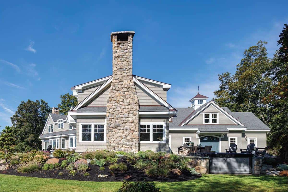 Rear of the house with a fieldstone chimney, cupola-topped wing, and outdoor kitchen on the patio